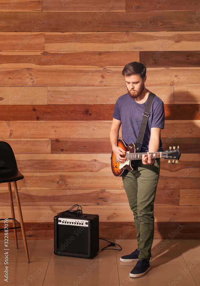 Young man playing guitar near wooden wall