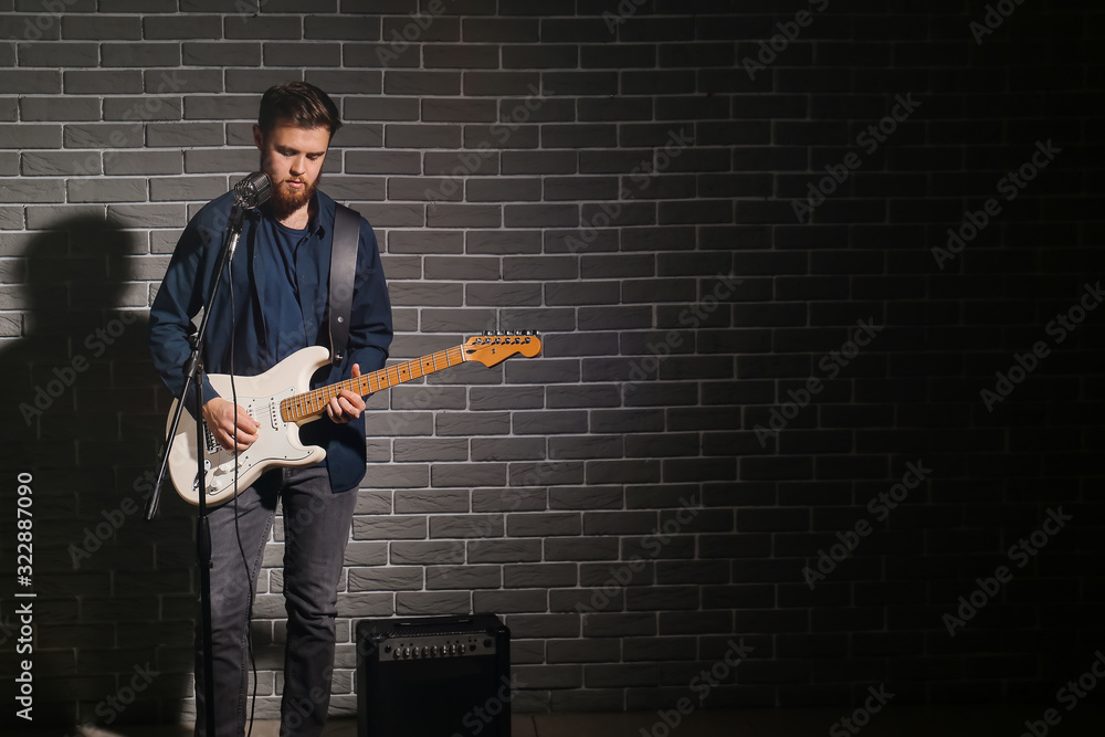 Young man playing guitar near dark brick wall