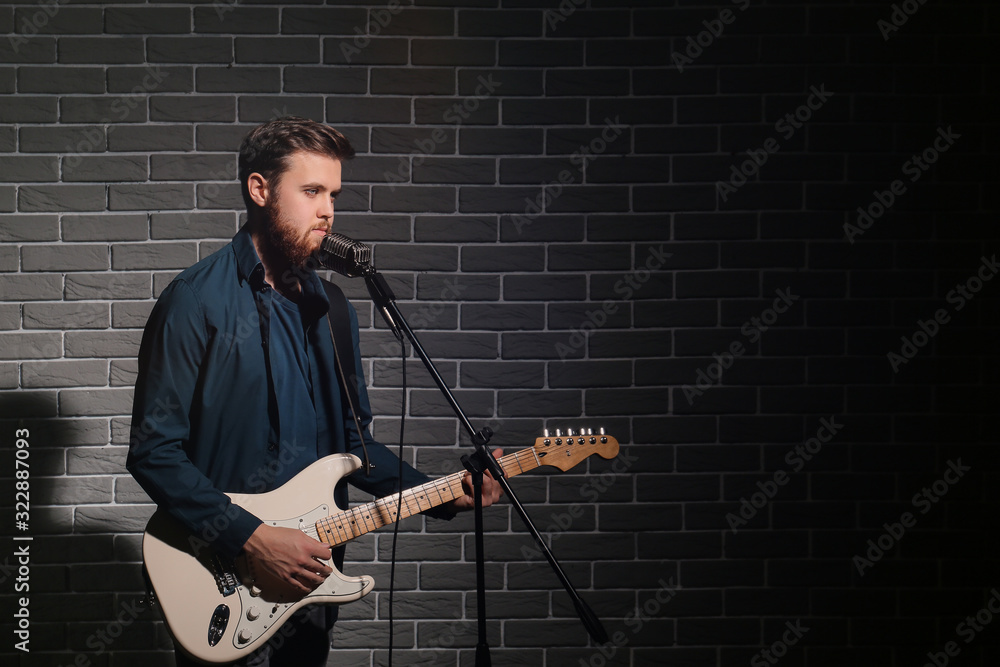 Young man playing guitar near dark brick wall