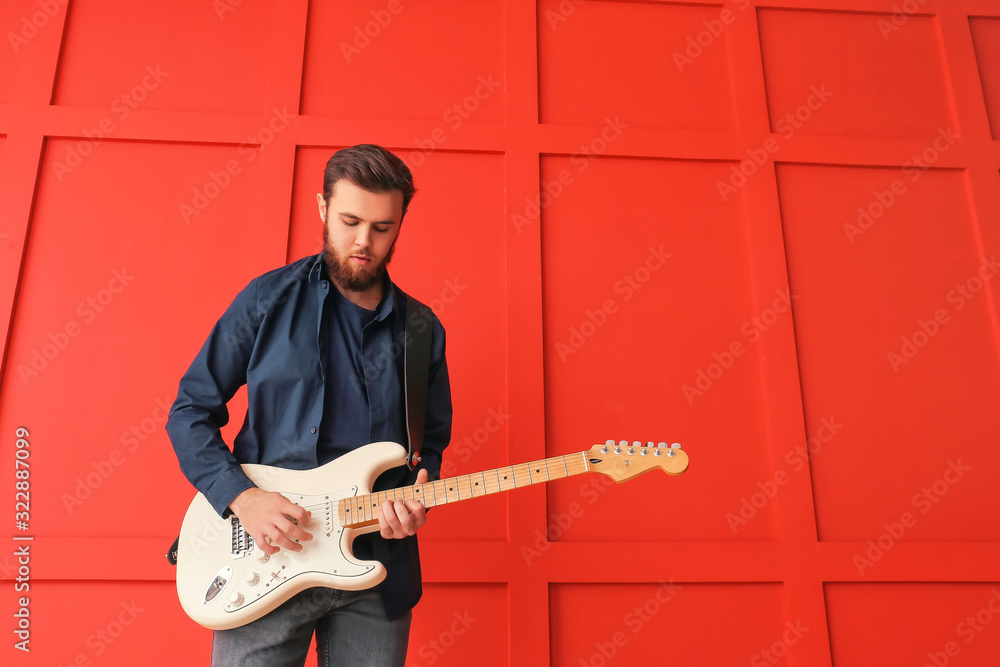 Young man playing guitar near color wall