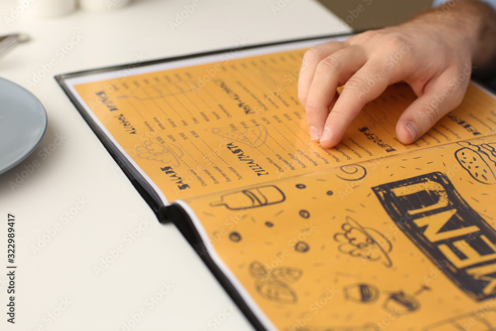 Young man with menu sitting in restaurant, closeup