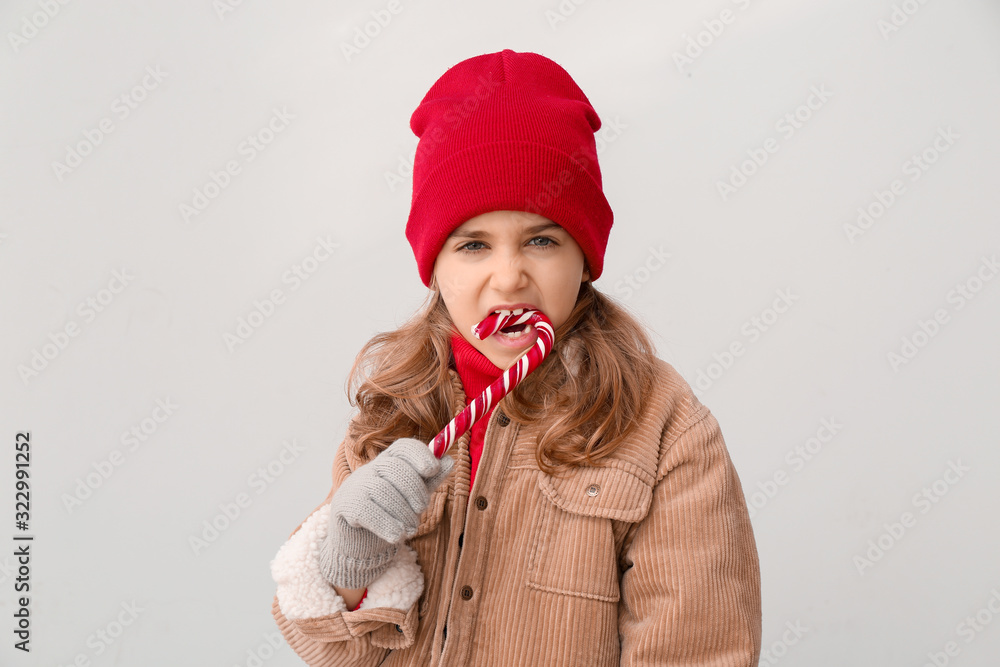 Cute little girl in winter clothes and with candy cane on light background