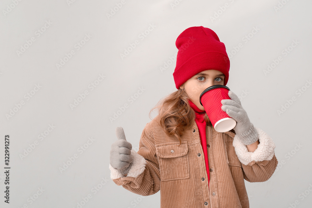 可爱的小女孩，穿着冬装，手里拿着一杯热巧克力，在灯b上做拇指向上的手势