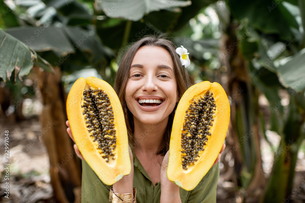 Portrait of a young woman with sliced papaya fruit on the plantation. Concept of vegetarianism, heal