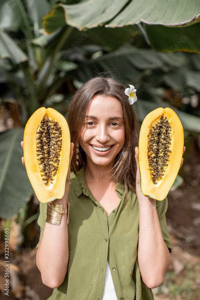 种植园里一个年轻女人拿着木瓜切片的肖像。素食主义的概念，治愈