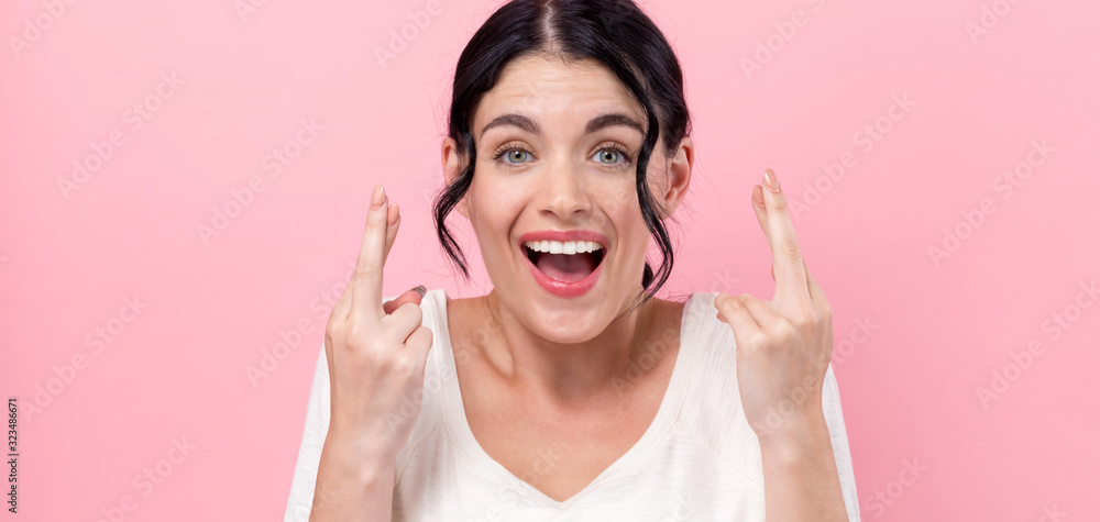 Young woman crossing her fingers and wishing for good luck on a pink background