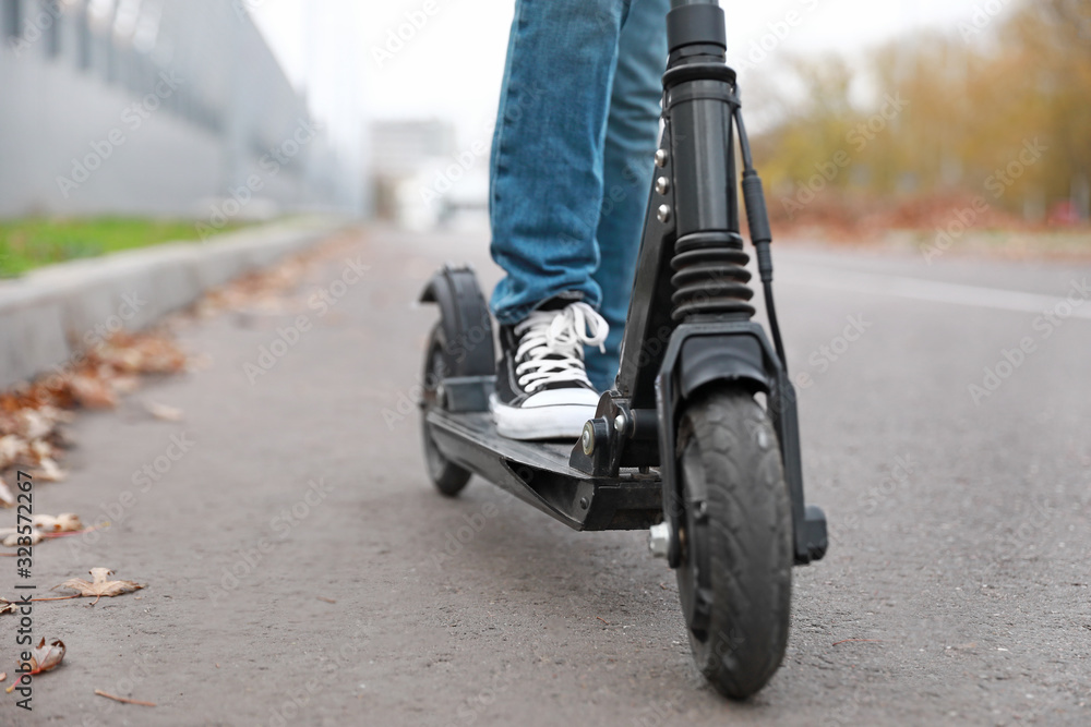 Teenage boy riding kick scooter outdoors, closeup