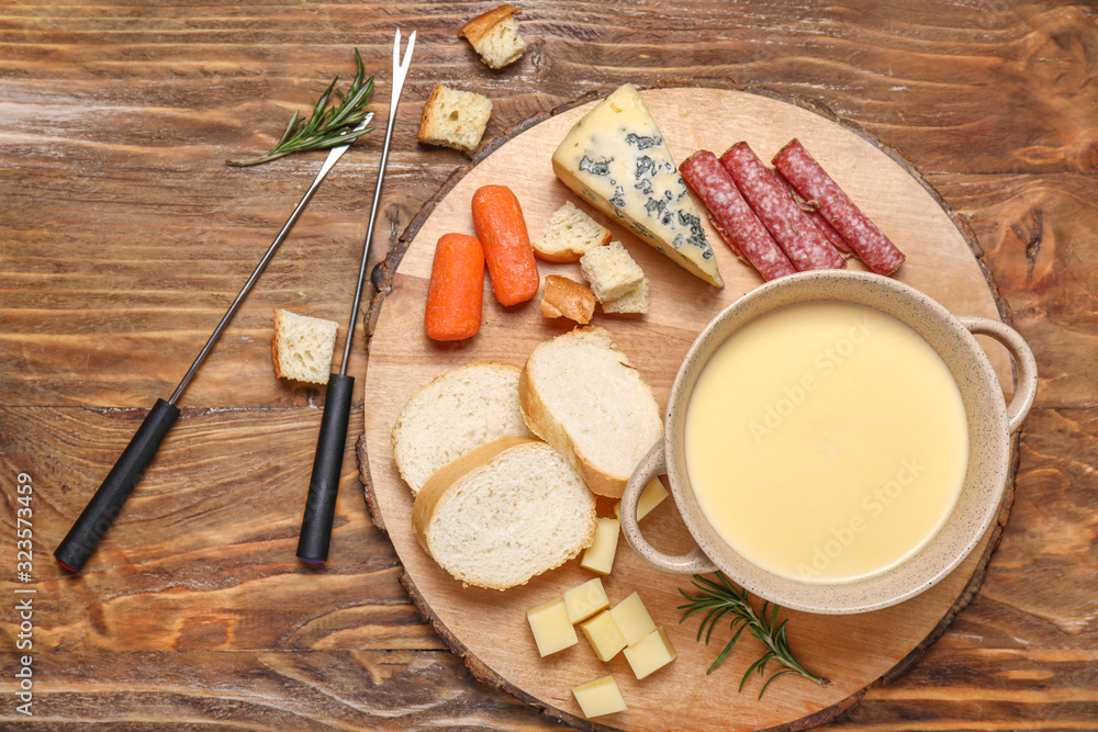 Cheese fondue with snacks on wooden background