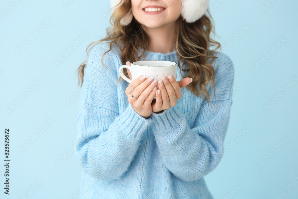 Beautiful young woman in warm sweater and with hot tea on color background