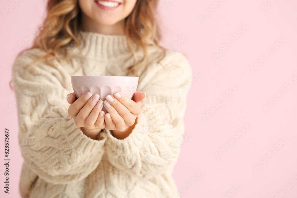 Beautiful young woman in warm sweater and with hot tea on color background