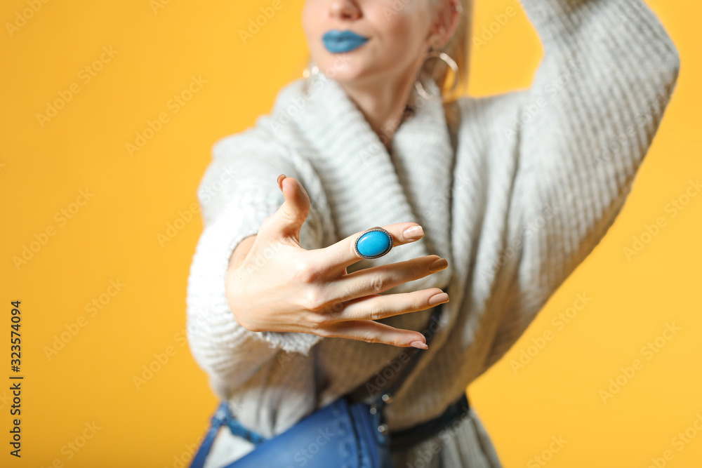 Young woman in warm sweater and with stylish ring on color background, closeup