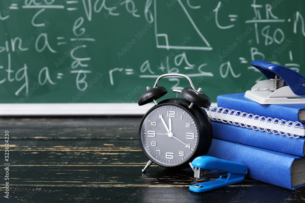 Set of school stationery and clock on table in classroom