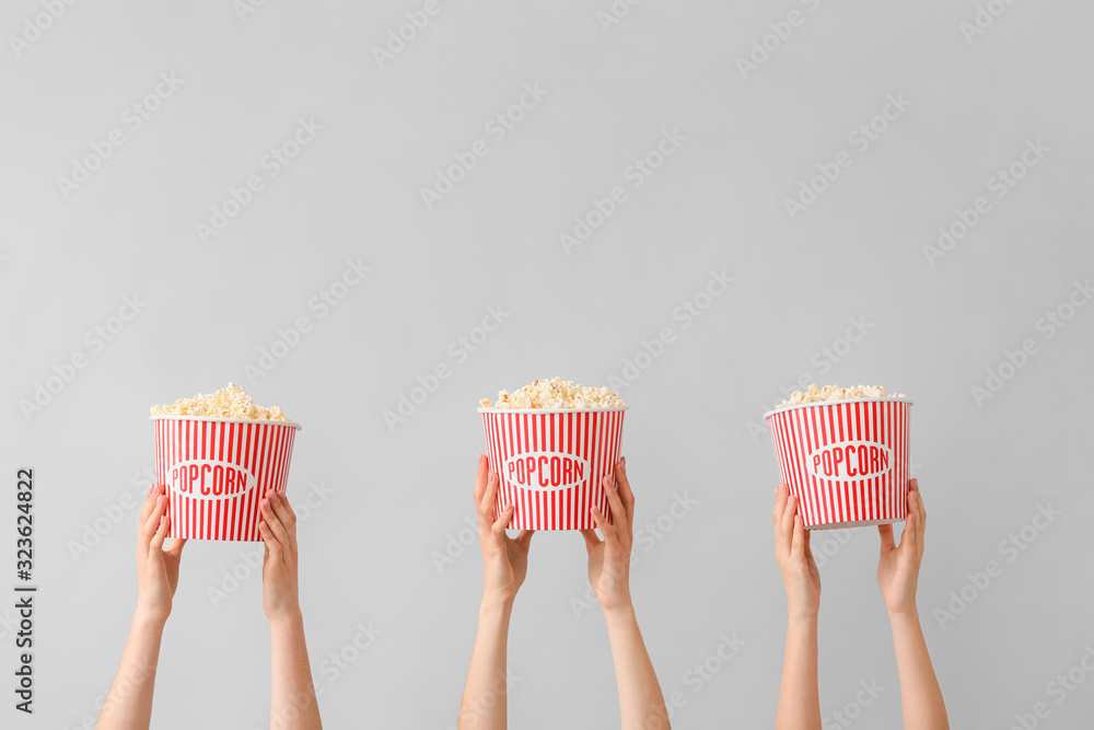 Many hands with popcorn in buckets on grey background