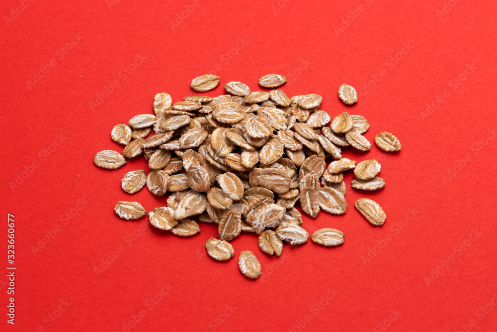 Pile of oat rye flakes on red color background