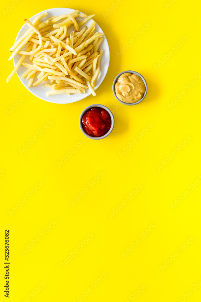 Fast food symbol. French fries on plate on yellow table top-down copy space