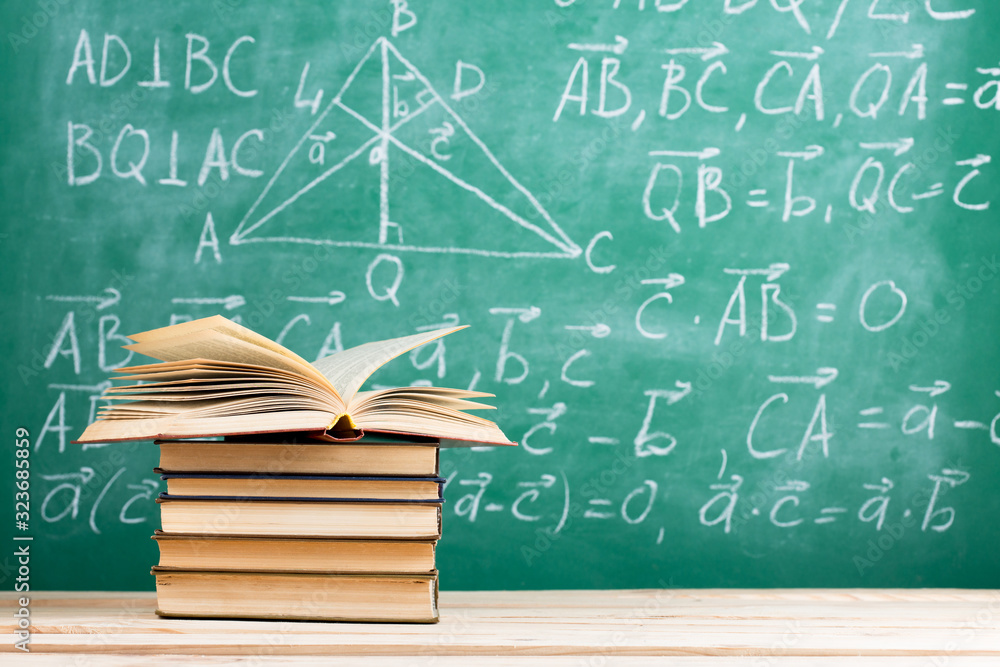 Education and reading concept - group of books on the wooden table, green blackboard with formulas o