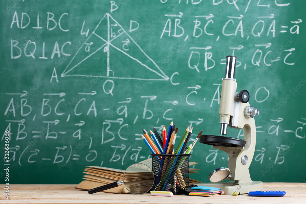 Education and sciences concept - books on the teacher desk in the auditorium, chalkboard on the back