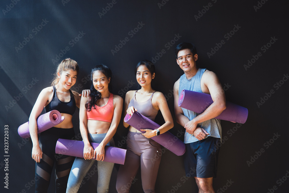 Group of asian young  people with yoga mats standing at Black wall. They smile happily. They have a 