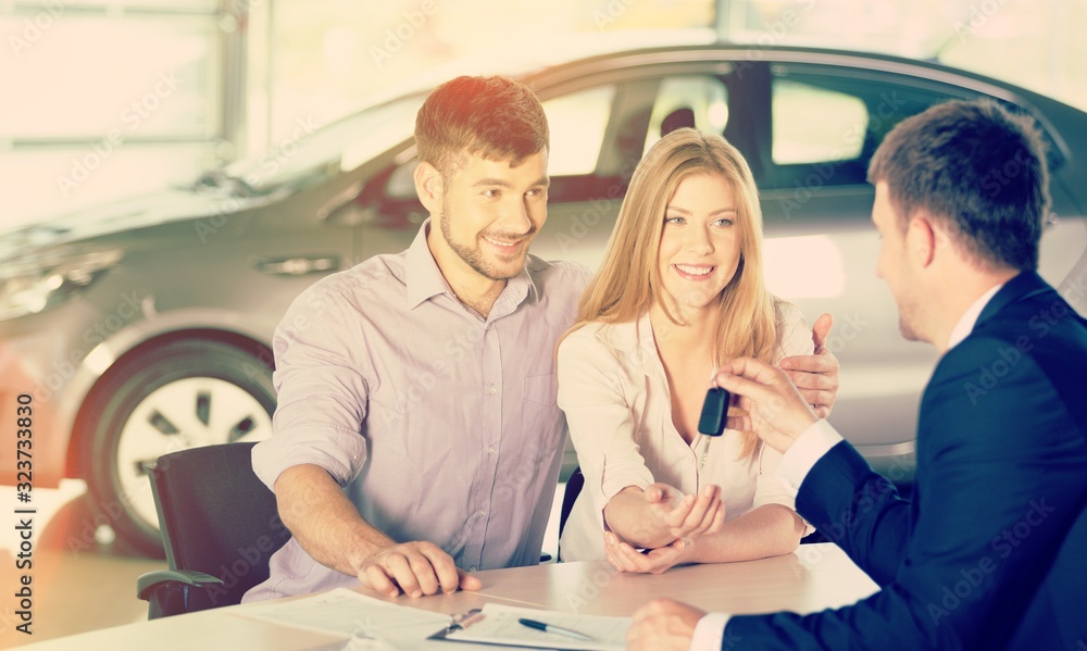 Happy couple with car dealer in auto show or salon