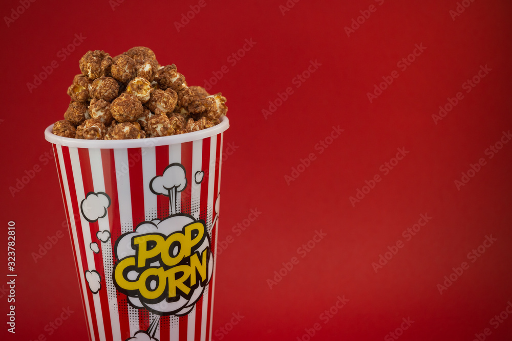 Butter popcorn in a red popcorn cup, snack in the house or cinema on a red background