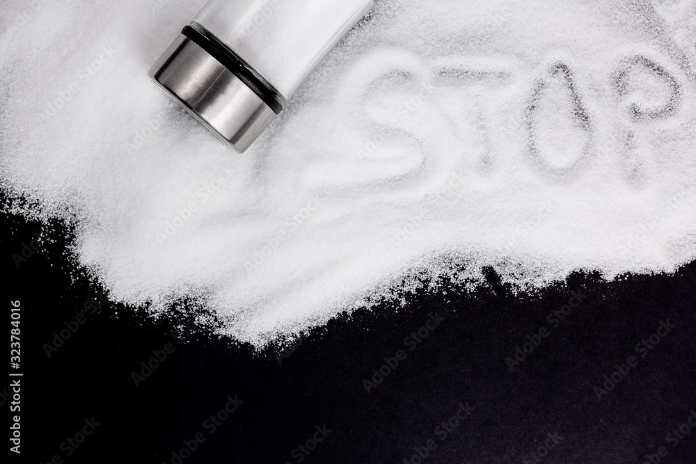 White sea salt for cooking in a small glass bottle. On the salt background, write stop. Concept for 