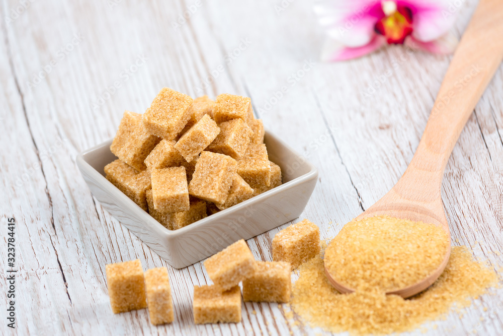 Brown sugar in a square cup and wooden spoon on a wooden table, healthy sugar is used for cooking fo