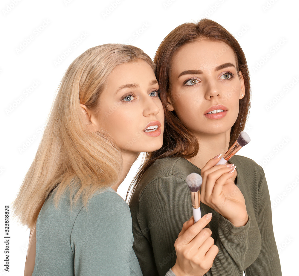 Beautiful young women with makeup brushes on white background