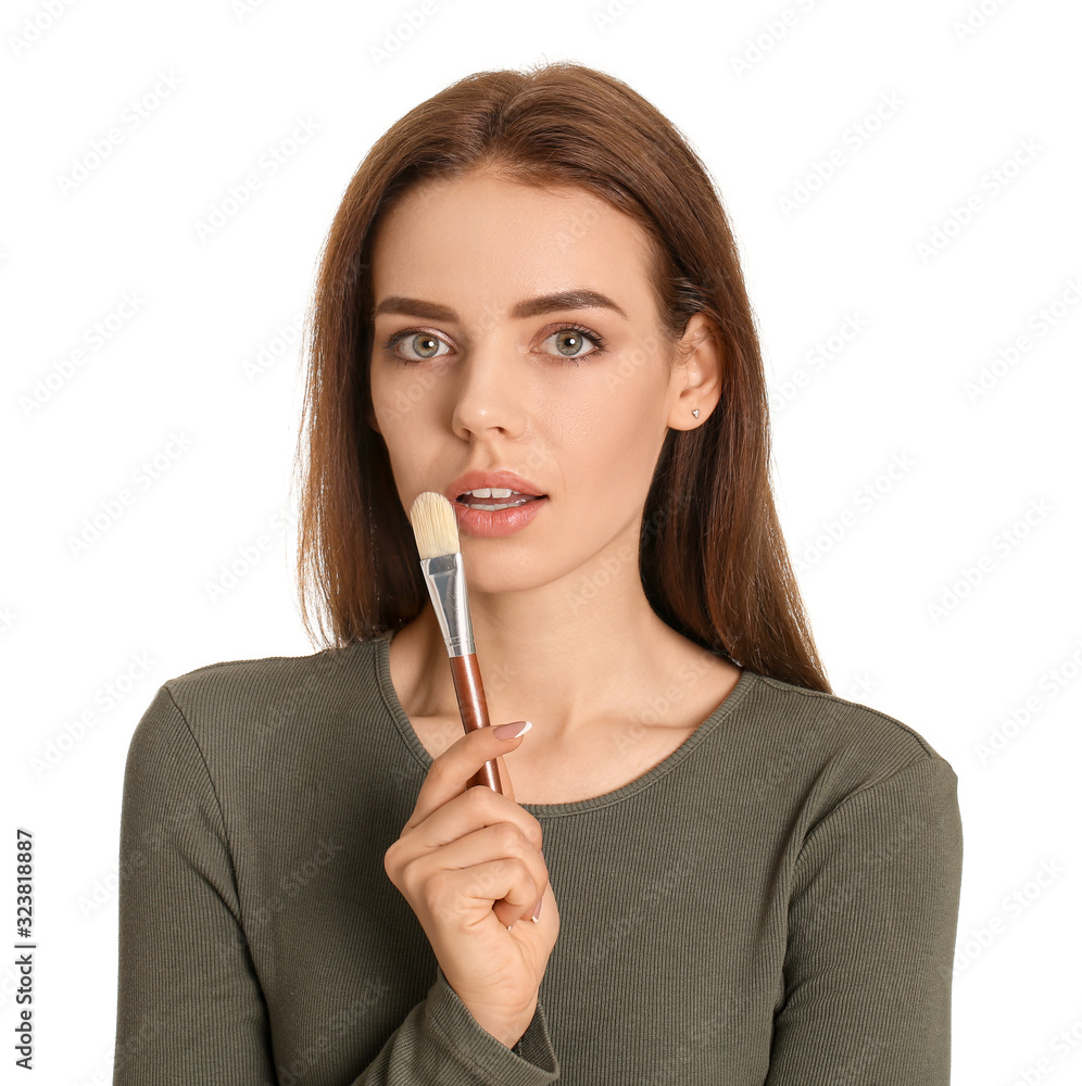 Beautiful young woman applying makeup on white background