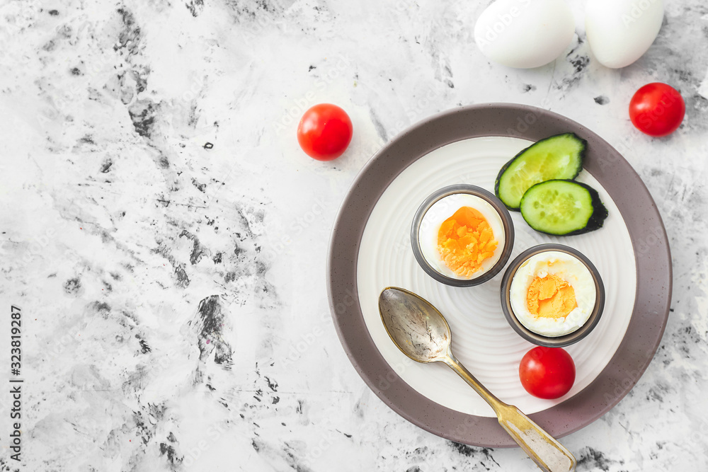 Plate with tasty boiled eggs and vegetables on light background