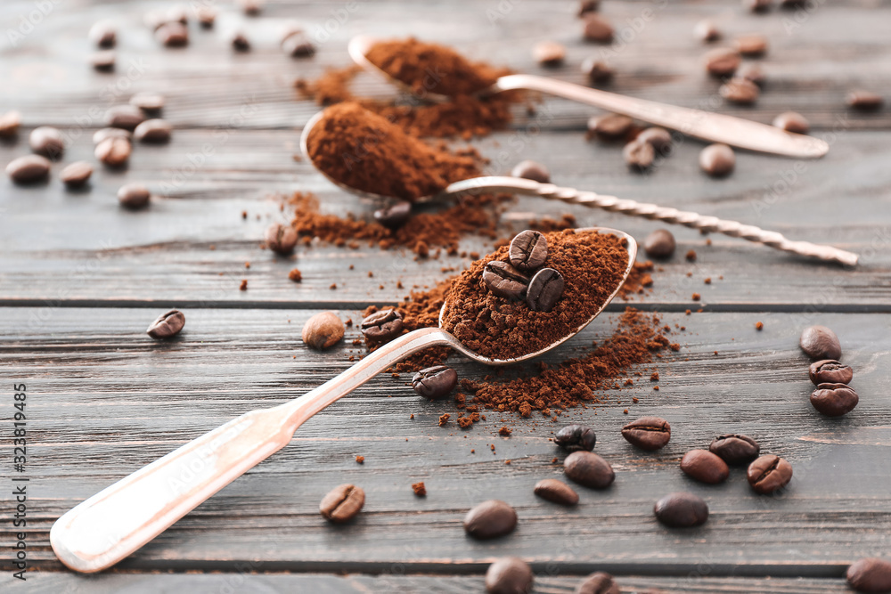 Spoons with coffee beans and powder on wooden background