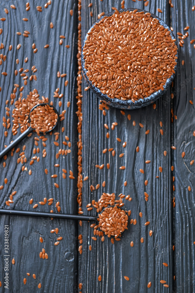 Bowl with flax seeds and spoons on wooden background