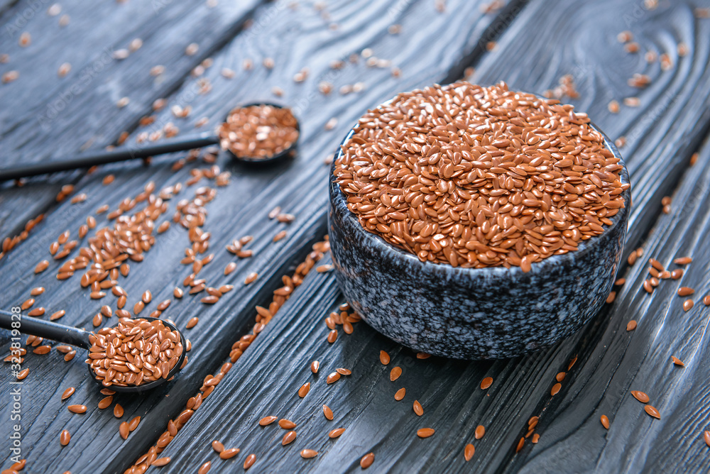 Bowl with flax seeds and spoons on wooden background