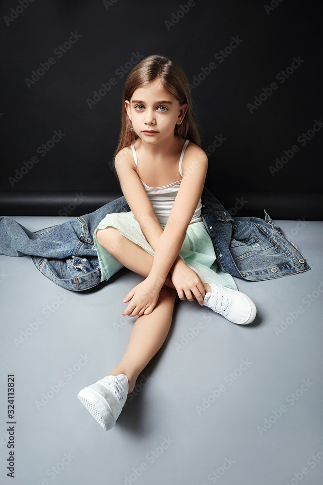 Cute fashionable girl sitting near dark background