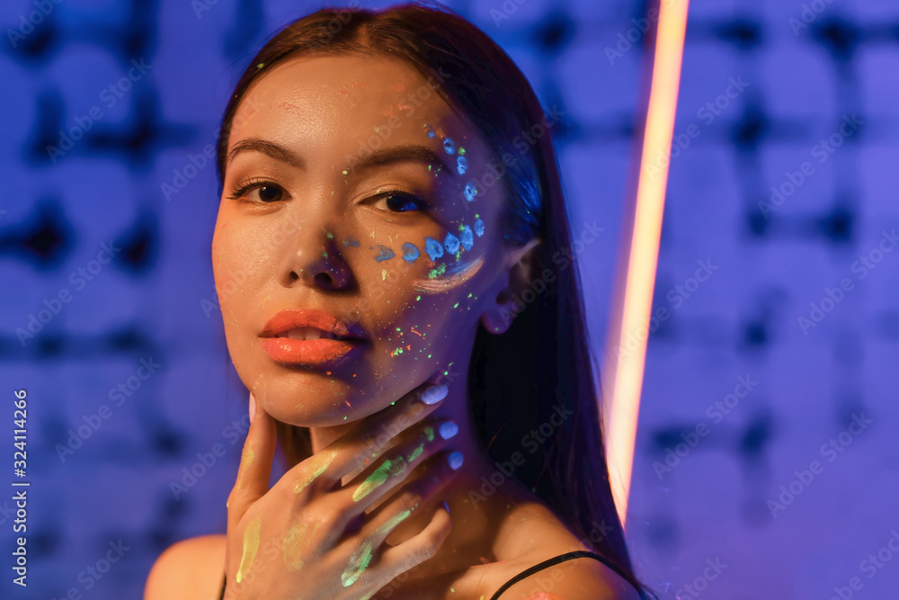 Young woman with fluorescent paint on her skin on color background