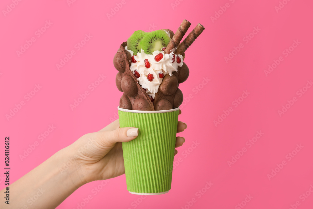 Female hand with delicious sweet bubble waffle on color background