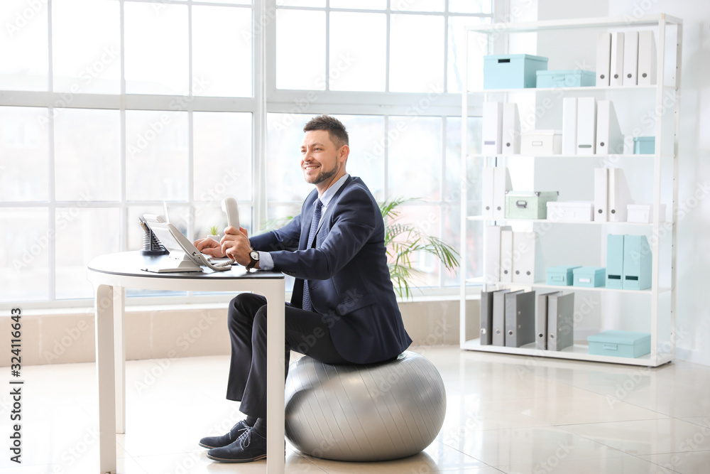 Businessman sitting on fitness ball while working in office