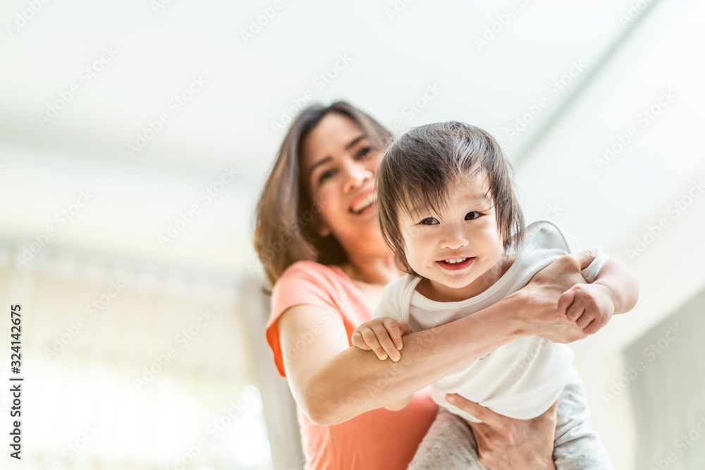 亚洲美女妈妈抱着可爱的婴儿，手臂像飞机一样摆动。孩子微笑着，享受玩耍