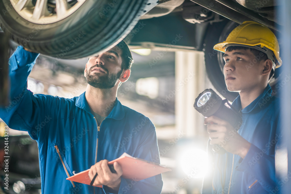 Vehicle service maintenance handsome mens checking under car condition in garage. Automotive mechani