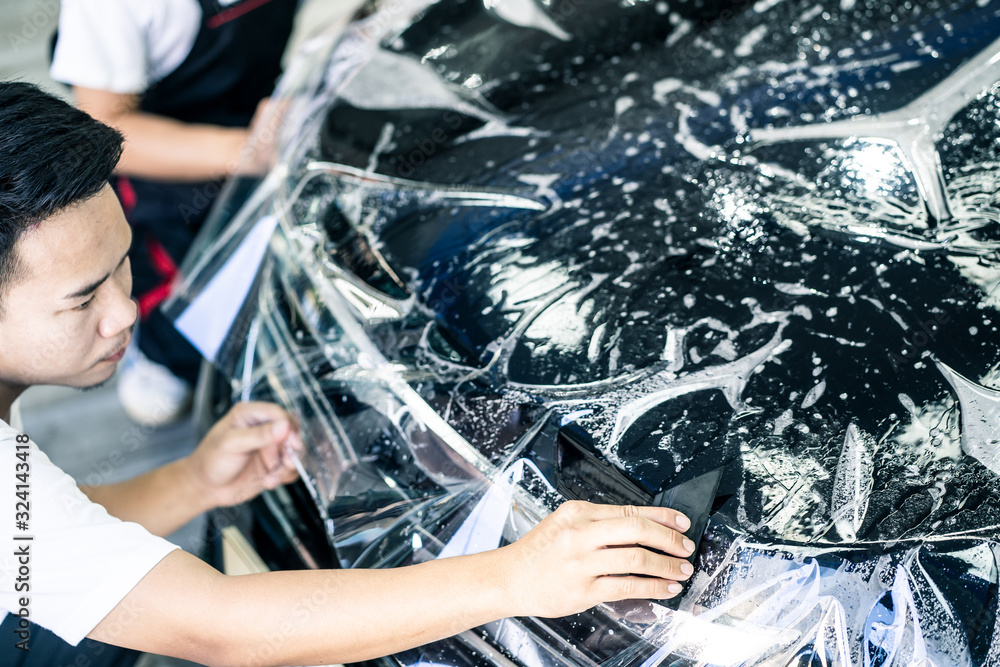 Focus on hand of worker holding film. Detailing of two Asian car film protection male worker install