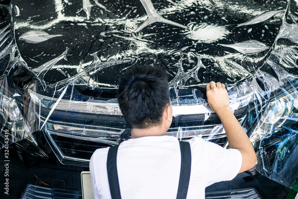 Focus on hand of worker holding film. Detailing of Asian car film protection male worker installing 