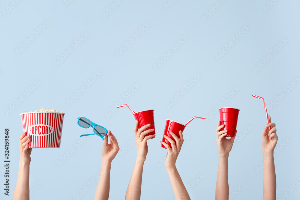 Many hands with popcorn, drink and eyeglasses on color background