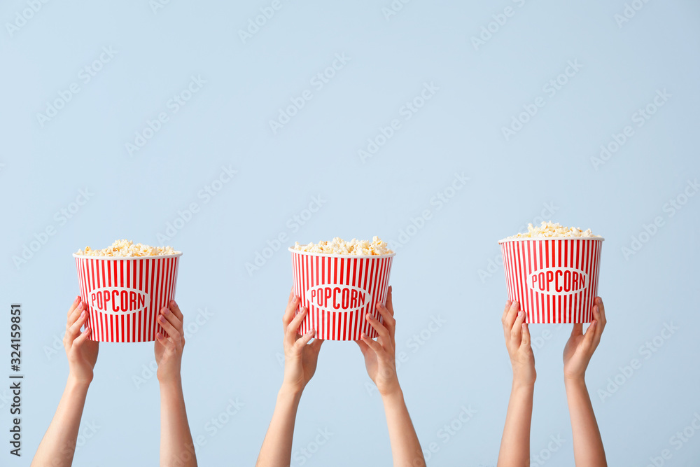 Many hands with popcorn in buckets on color background