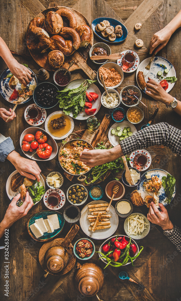 Turkish breakfast. Flat-lay of peoples hands taking and eating Turkish pastries, vegetables, greens,