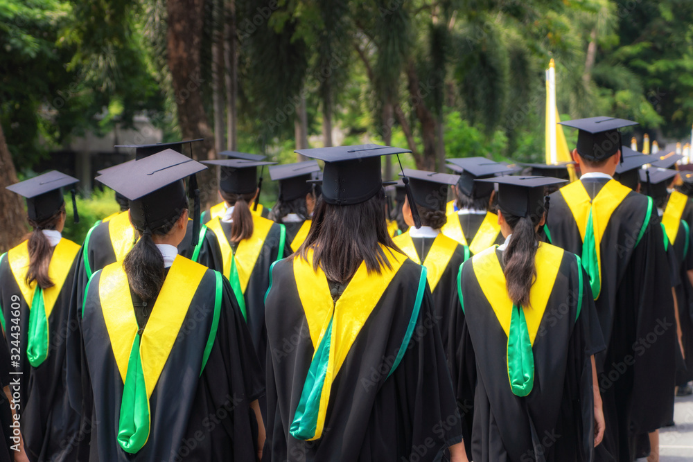 一群穿着黑色长袍的大学毕业生在大学毕业典礼上排队攻读学位的背影