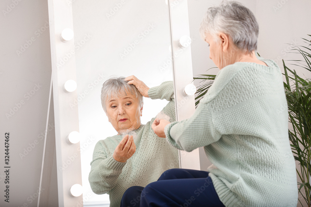 Senior woman with hair loss problem near mirror