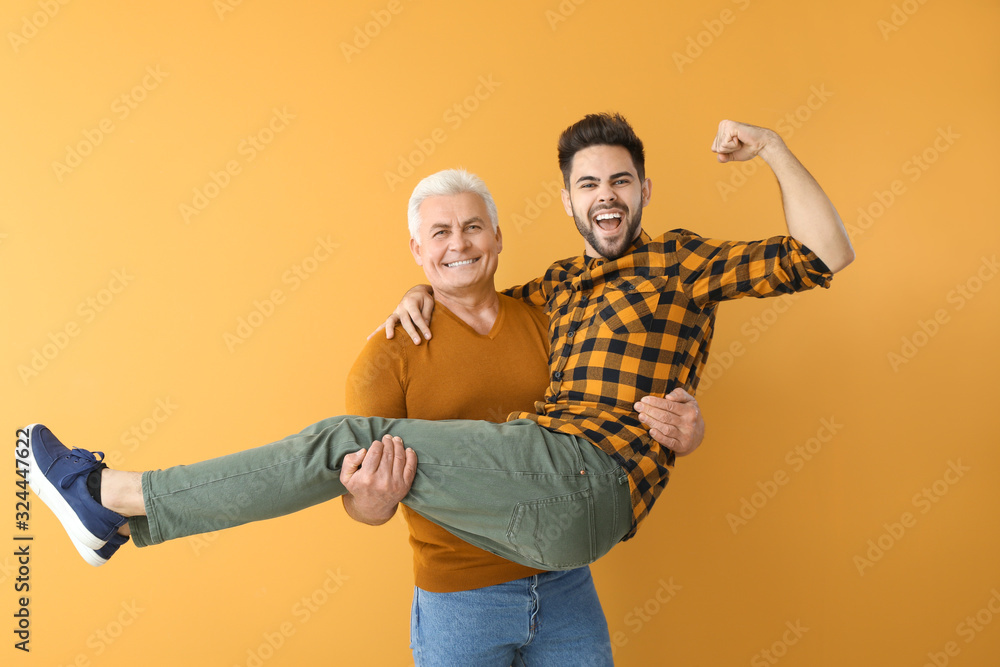 Young man and his father having fun on color background