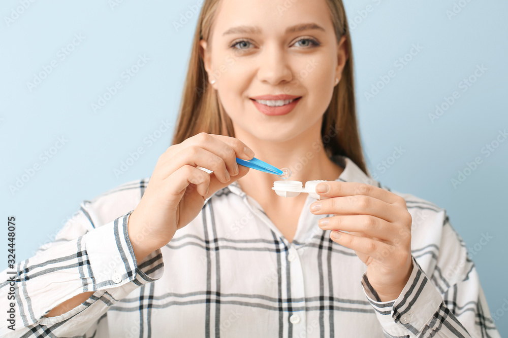 Young woman with contact lens case and tweezers on grey background