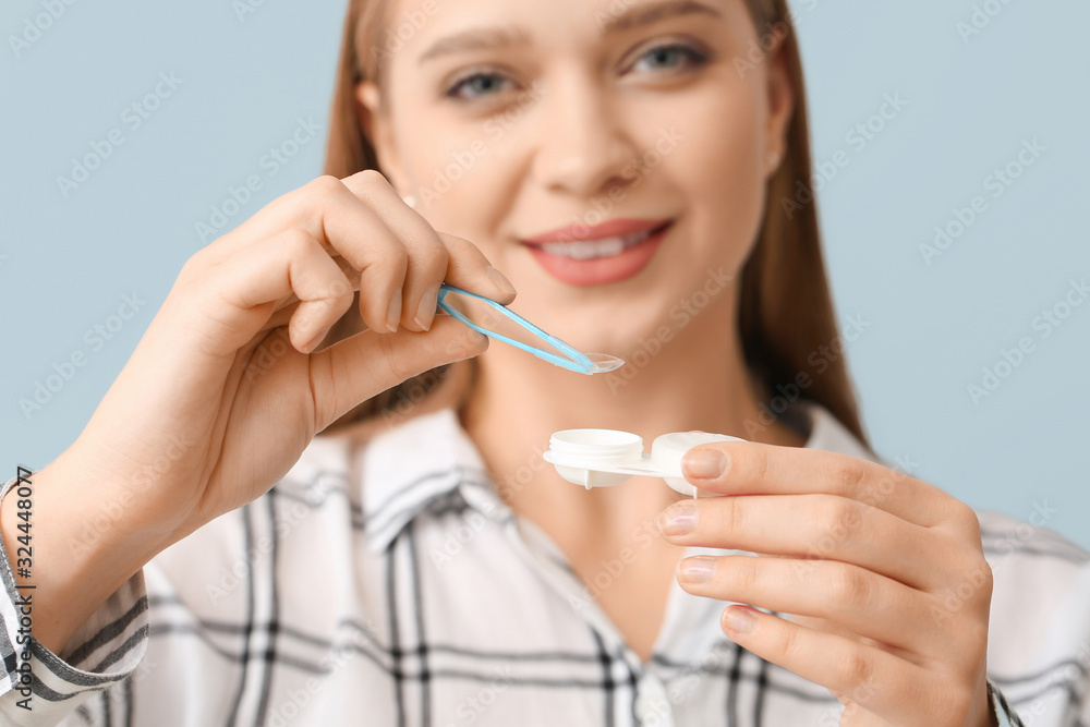 Young woman with contact lens case and tweezers on grey background, closeup