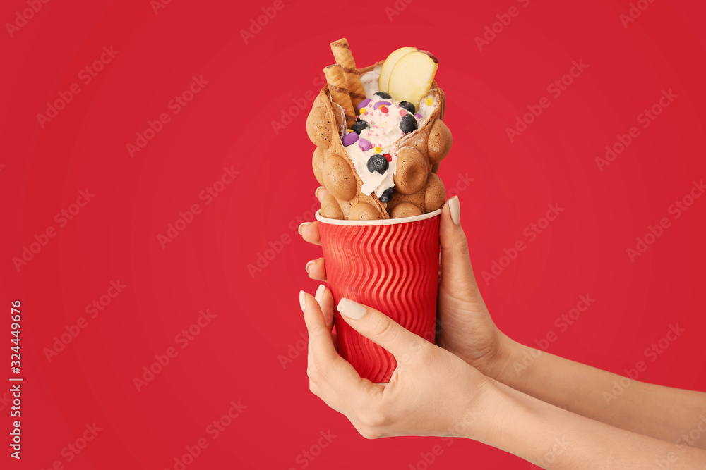 Female hands with delicious sweet bubble waffle on color background