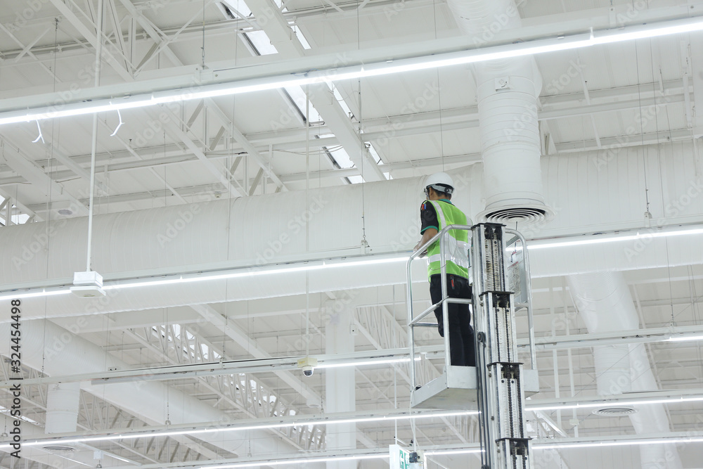 Unidentified male worker operating maintenance of warehouse lighting system